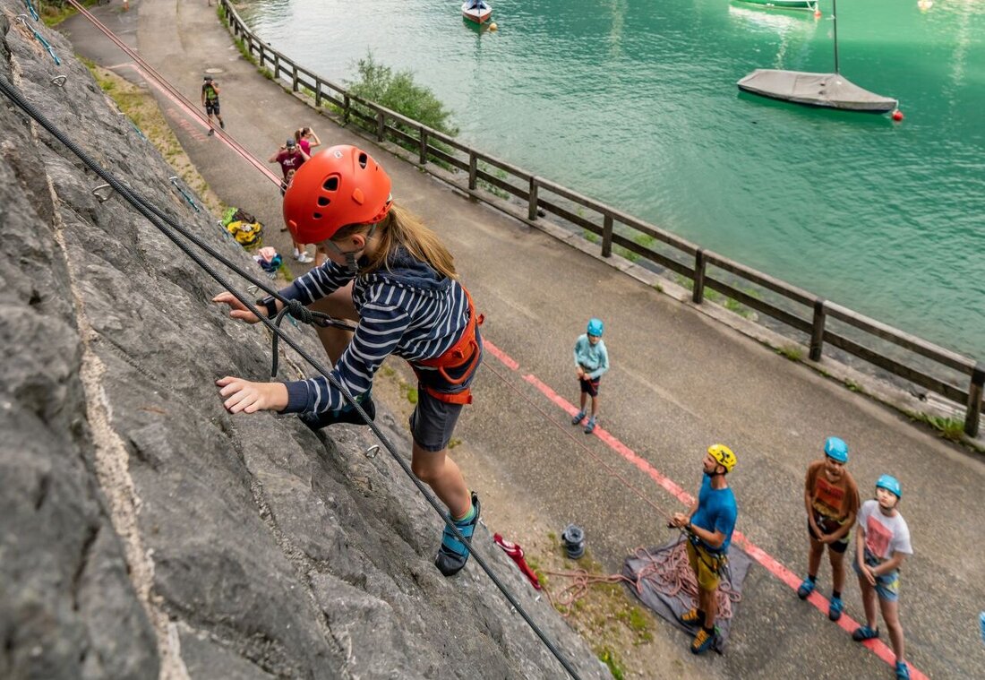 Kind klettert auf einer Felswand neben dem See