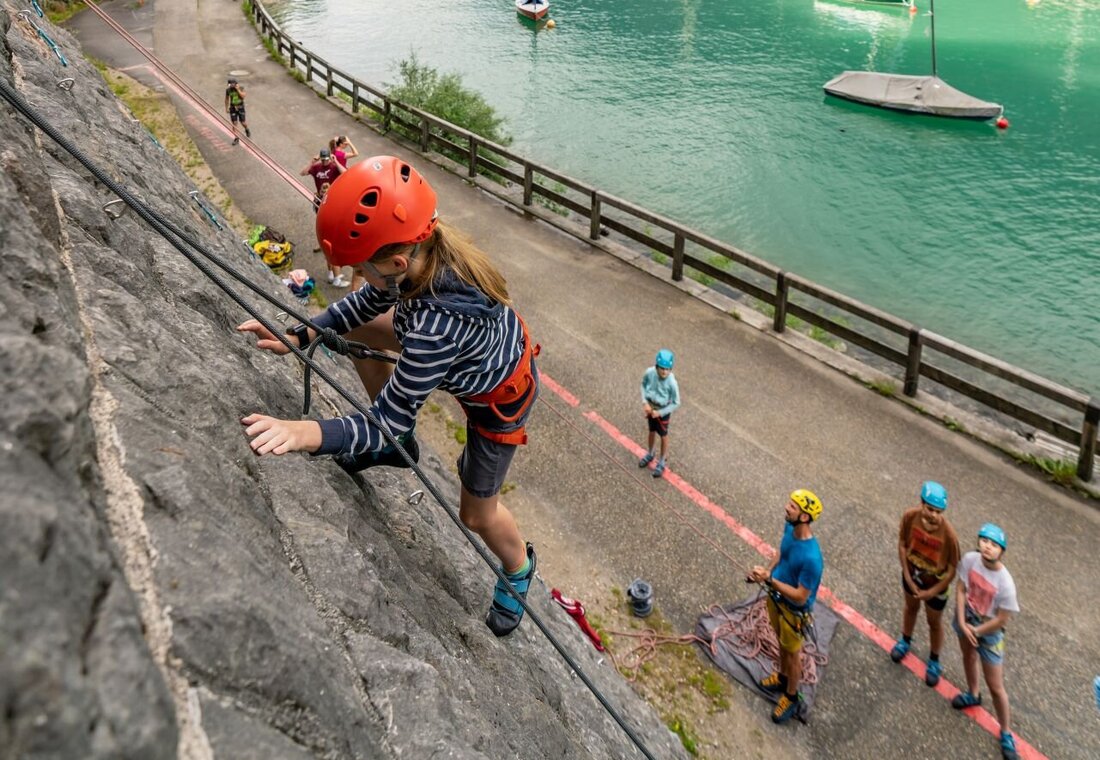 Kind klettert auf einer Felswand neben dem See