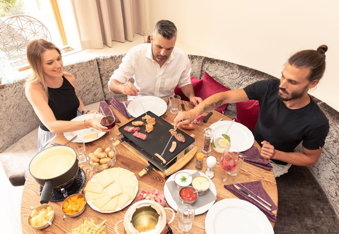 Zwei Männer und eine Frau sitzen an einem Tisch und essen Fondue und Raclette